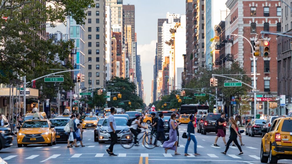 A busy city intersection with pedestrians crossing and cars waiting at a traffic light.