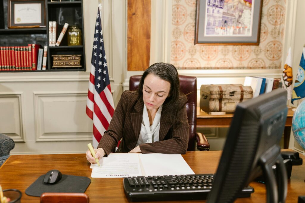 Female attorney in a law office signing legal documents at her desk, surrounded by legal books and symbols of justice.