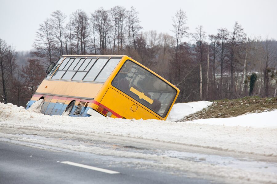 A yellow bus partially submerged in snow off the side of a road.