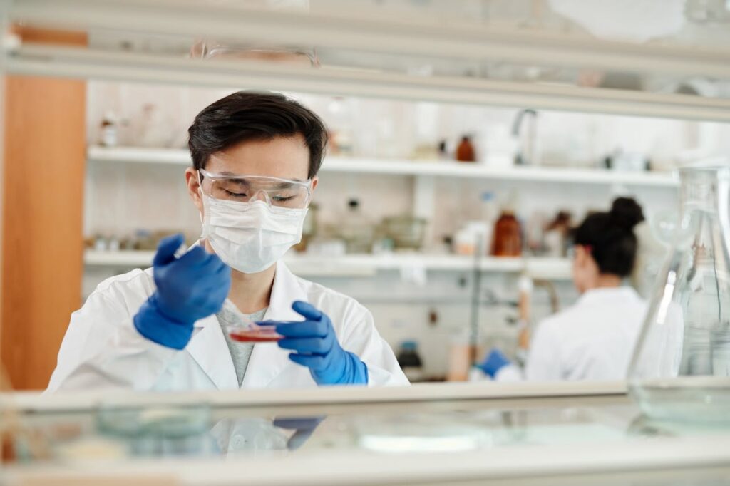 A scientist wearing a mask and gloves working with a petri dish in a laboratory.